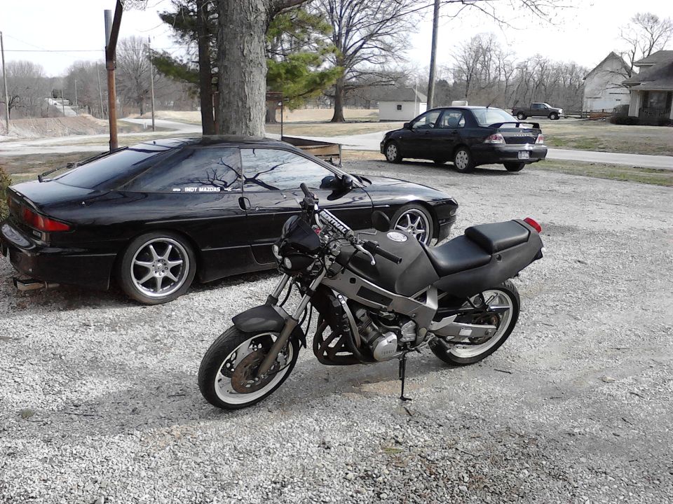 Black 1995 Ford Probe parked next to a motorcycle, with another car in the background