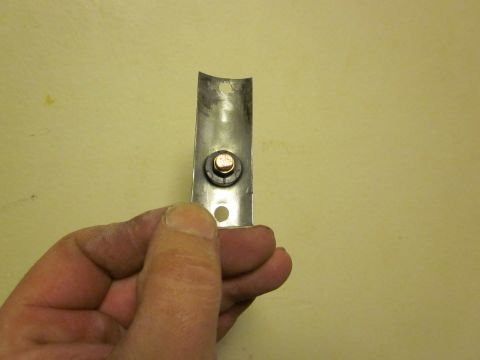 1979 Ford Bronco - A metal bracket with a bolt is held by a hand in front of a yellow wall.