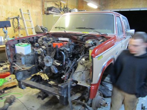 1984 Ford Bronco - This red and tan Ford Bronco is undergoing engine work, with the engine removed from the bay.