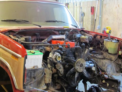 1984 Ford Bronco - The engine bay of a red and tan SUV is shown with the engine partially disassembled and removed.