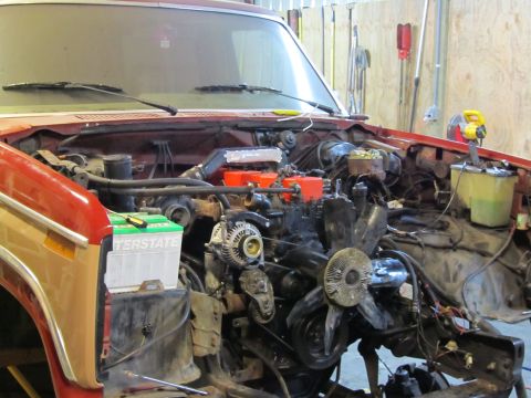 1984 Ford Bronco - The engine bay of a red vehicle is shown with the engine exposed and an Interstate battery in place.