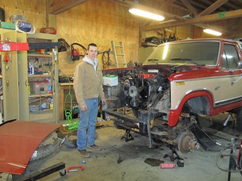 1984 Ford Bronco - A 1984 Ford Bronco is disassembled in a garage, with its engine bay open and front end raised on jack stands.