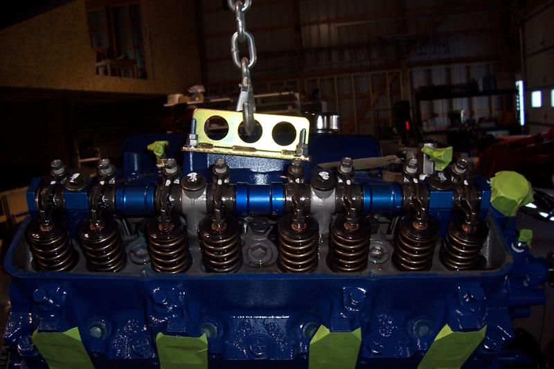 Blue V8 engine on chain hoist with valve cover removed showing rocker arms and valve springs