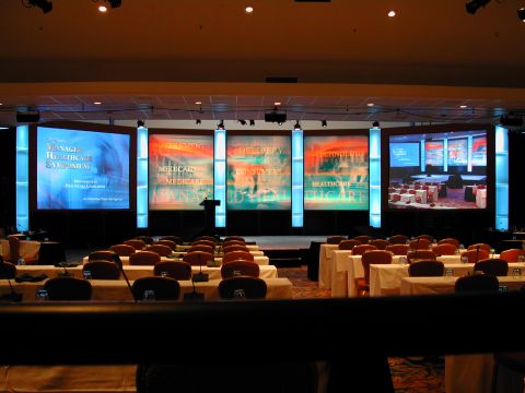 1994 Ford Bronco - A conference room is set up with rows of tables and chairs facing a stage multiple large screens displaying text related to healthcare.