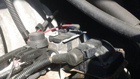 1994 Ford Bronco - Tight engine-bay shot of black electrical connectors and loom-wrapped harness branches plugging into a sensor and an ignition coil pack, wi…