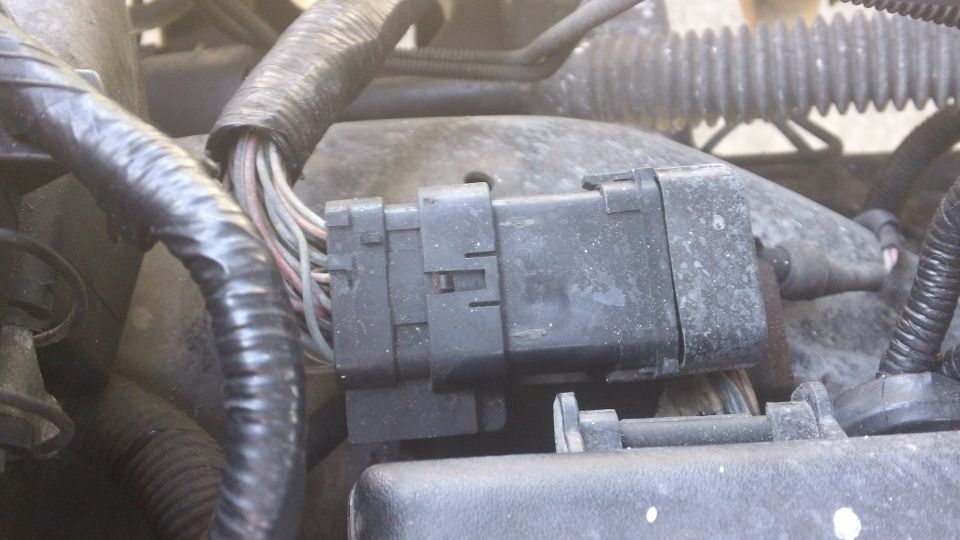 Close-up of a black electrical connector with multiple wires going into it, part of a vehicle's engine bay