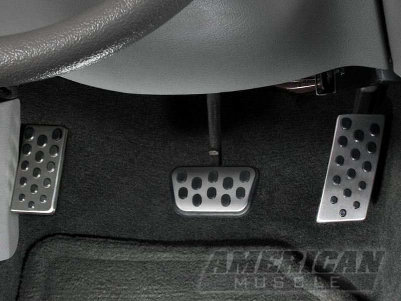 Aftermarket aluminum pedal covers on black carpet with a partial dashboard visible