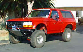 1990 Ford Bronco - A red 1990 Ford Bronco is parked outdoors, showing its front-right side with modifications.