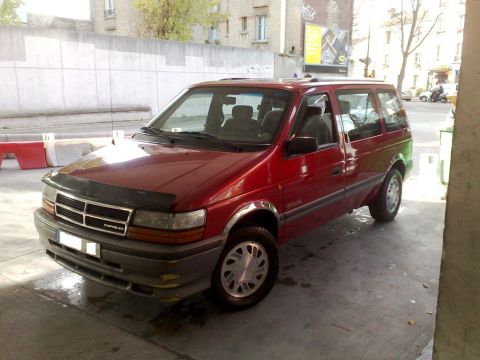 1991 Ford Crown Victoria - A red minivan is parked under an overhang, showing its front and side profile.