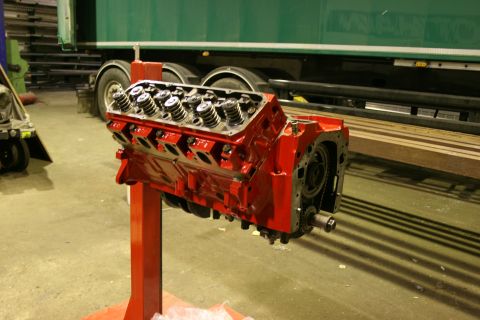 1973 Ford Ranchero - A freshly painted V8 engine block is displayed on a red stand in a workshop.