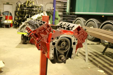 1973 Ford Ranchero - A red V8 engine block is displayed on a stand, showing its internal timing gears, within a workshop environment.