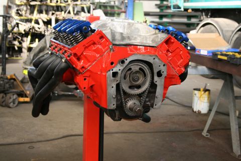 1973 Ford Ranchero - A red Ford V8 engine with blue valve covers and black headers is displayed on a stand in a workshop.