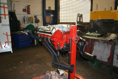 1973 Ford Ranchero - A V8 engine assembly with custom headers sits on a stand in a workshop environment.