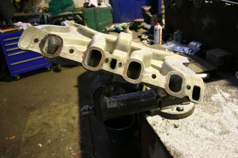 1973 Ford Ranchero - Engine intake manifold clamped in a vise, ready for work. The Supermotors logo is visible in the lower right.