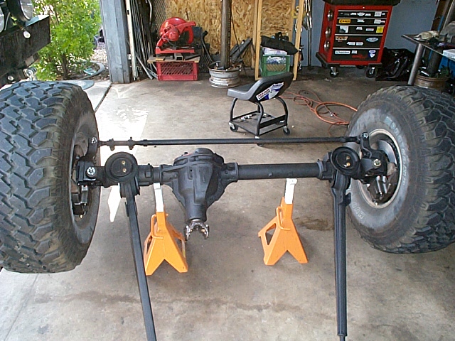 Front axle on jack stands with mud tires and radius arms in a garage