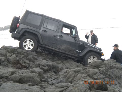 2005 Jeep Wrangler - A black Jeep Wrangler Rubicon navigates a rocky terrain near the water.
