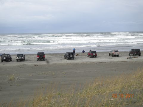 2005 Jeep Wrangler - A group of Jeep Wranglers are seen on the beach near the ocean on a cloudy day.