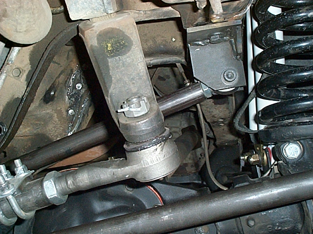 Underbody close-up of tie rod end, coil spring, and rusty mounting bracket