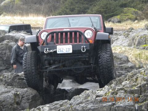 2005 Jeep Wrangler - A red Jeep Wrangler is shown off-roading on a rocky path, with another vehicle visible in the background.