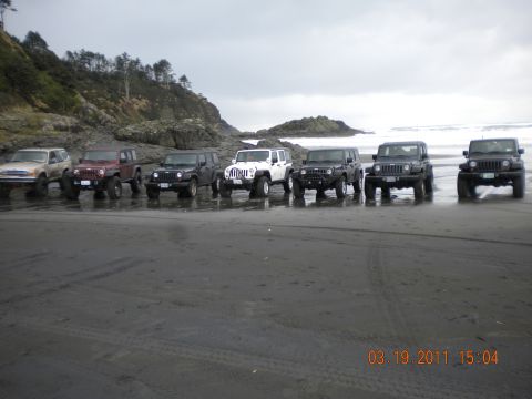 2005 Jeep Wrangler - A group of Jeep Wranglers are lined up on a sandy beach under an overcast sky.