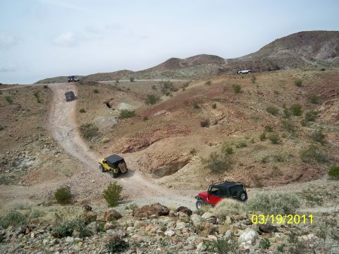 1992 Jeep Wrangler - Multiple Jeeps navigate a dusty trail through a desert landscape under a cloudy sky.