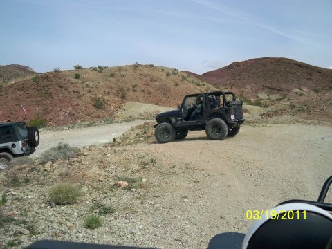 1992 Jeep Wrangler - Two Jeeps navigate a dusty trail through a rocky, arid terrain under a clear sky.