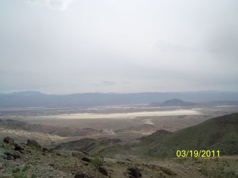 1992 Jeep Wrangler - A vast desert landscape unfolds under a cloudy sky, with mountains in the distance and a dry lake bed in the foreground.
