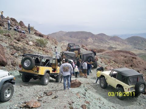 1992 Jeep Wrangler - Multiple off-road vehicles and people gathered on a , colorful hillside with mountains in the background.