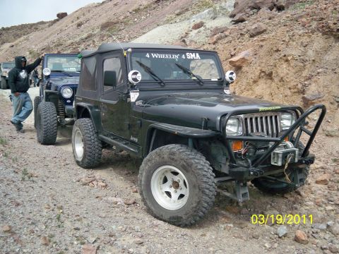 1992 Jeep Wrangler - A line of Jeeps, including a modified black 1992 Jeep Wrangler, navigate a rocky trail.