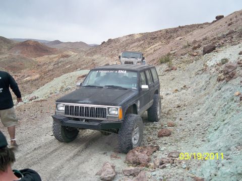 1992 Jeep Wrangler - A black Jeep Cherokee XJ navigates a rocky, off-road trail, with another Jeep visible in the distance. The date stamp reads 03/19/2011.