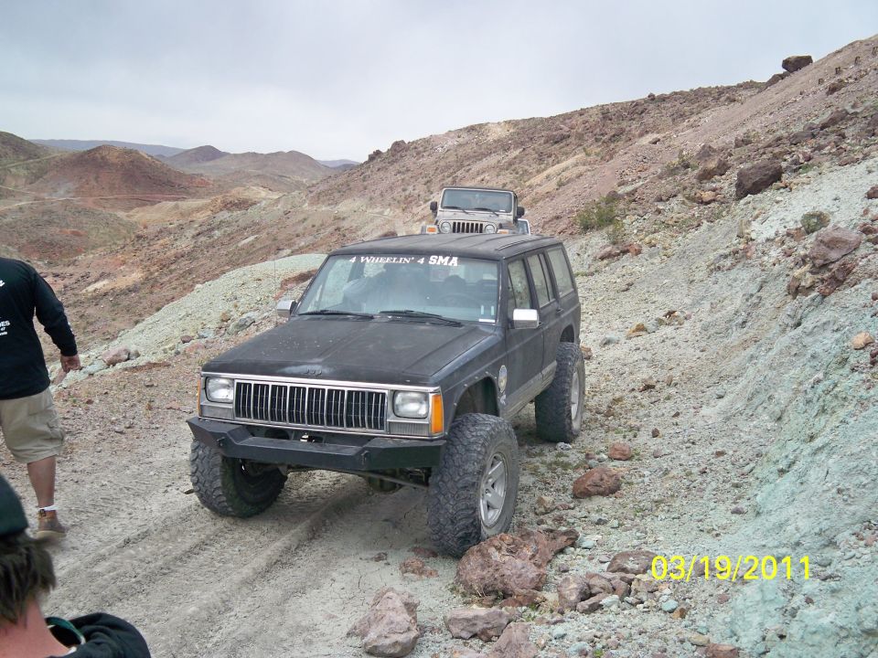 Black Jeep Cherokee XJ with aftermarket bumper, off-roading with another Jeep in background