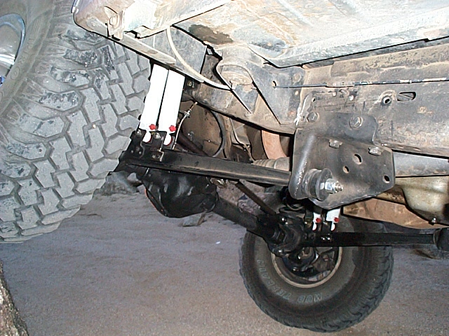 Underside of Ford Bronco front suspension with white straps and mud-terrain tire