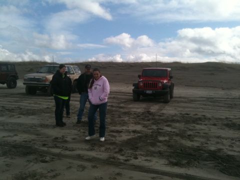 2005 Jeep Wrangler - Several vehicles and people gathered on a sandy beach under a cloudy sky.