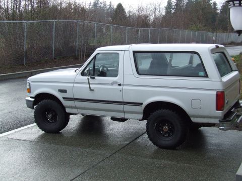 1996 Ford Bronco - A white Ford Bronco SUV is parked on a wet paved surface, viewed from the side.