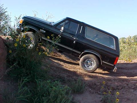 1989 Ford Bronco - This 1989 Ford Bronco is shown navigating an off-road trail with a clear blue sky above.