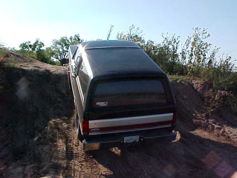 1989 Ford Bronco - This black Ford Bronco with a camper shell is captured from the rear as it navigates a dirt incline.