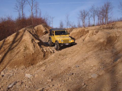 2003 Jeep Wrangler - A yellow Jeep Wrangler navigates a challenging dirt path with steep inclines and rocky terrain.