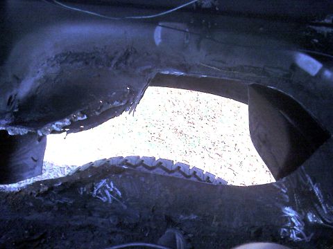 1992 Ford C-350 (Centurion Conversions) - The underside of a vehicle shows significant rust and a large opening, exposing the tire and exterior.