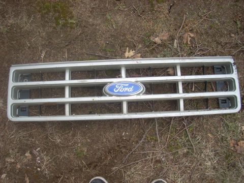 1996 Ford Bronco - A silver Ford grille with a blue oval emblem is shown lying on the ground.