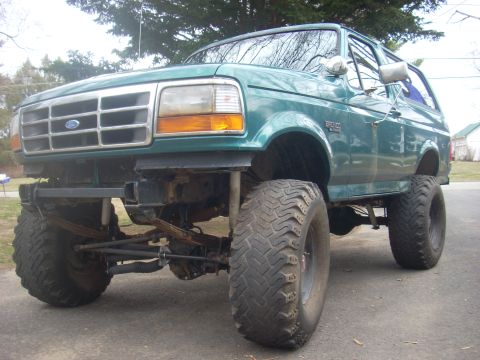 1996 Ford Bronco - A lifted green Ford Bronco sits parked on a paved surface, its large off-road tires and modified suspension.