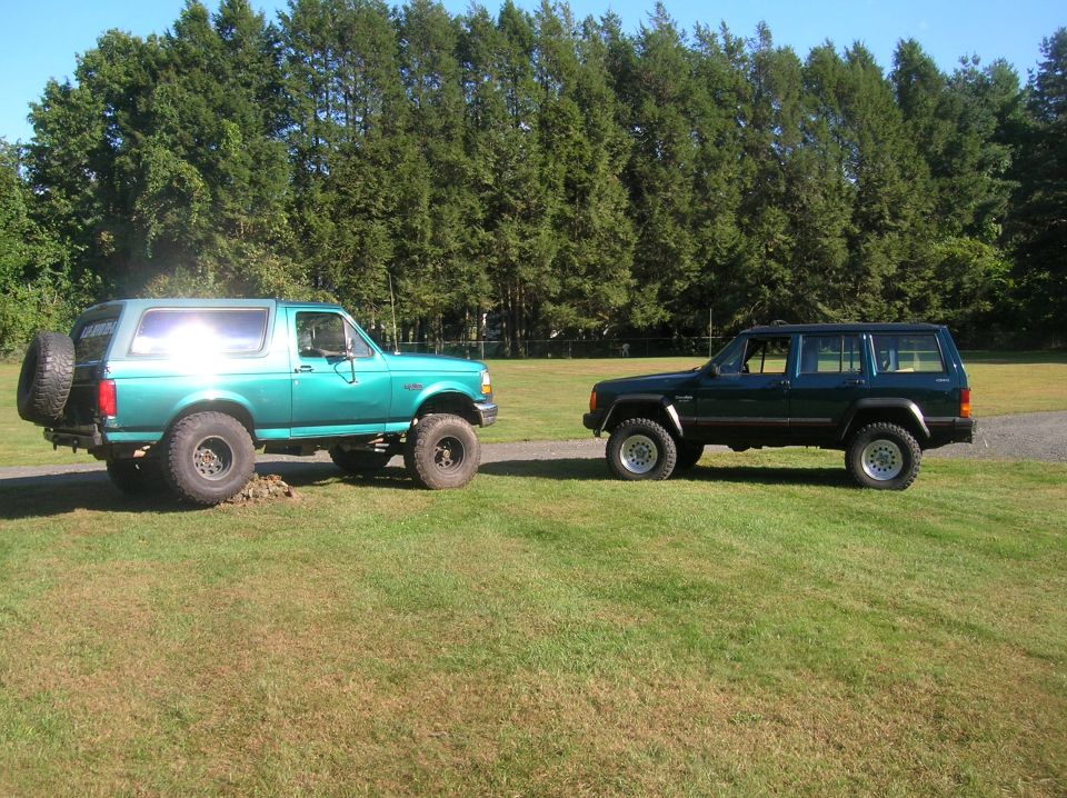Green 1995 Jeep Cherokee parked on grass next to a teal Ford Bronco