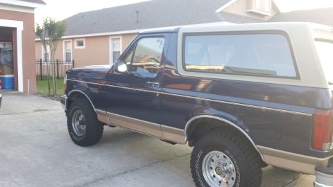 1994 Ford Bronco - Driver-side profile of a two-tone dark blue and tan Ford Bronco full-size SUV parked in a residential driveway, with the tan removable hard…