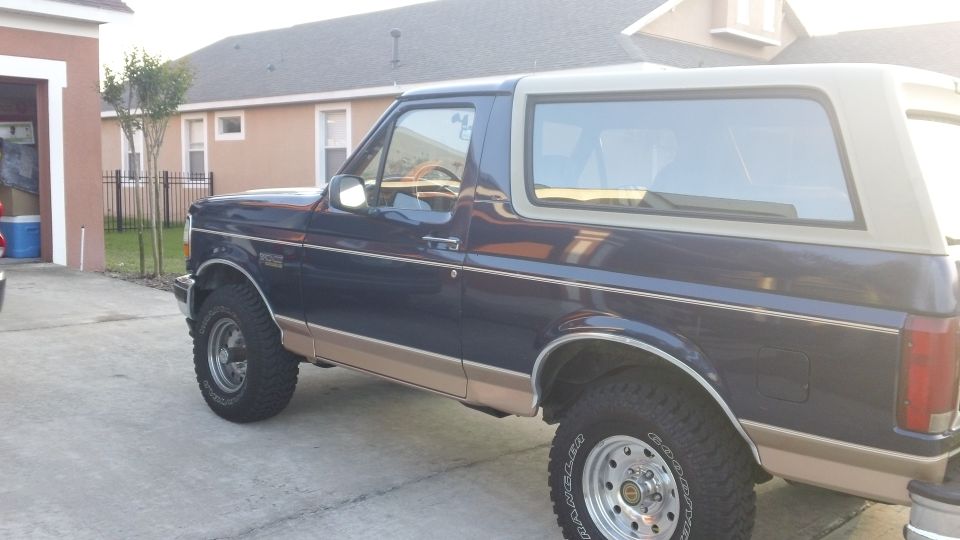 Blue and tan Ford Bronco SUV side profile in driveway on all-terrain tires