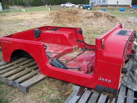 1992 Jeep YJ - The red body of a Jeep Wrangler sits on wooden pallets in a yard, with a house and tractor in the background.