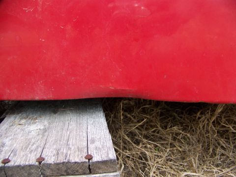 1992 Jeep YJ - Close-up view of a red vehicle panel supported by weathered wooden planks.