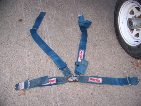 1992 Jeep YJ - A blue Simpson racing seatbelt is laid out on a concrete surface next to a tire.
