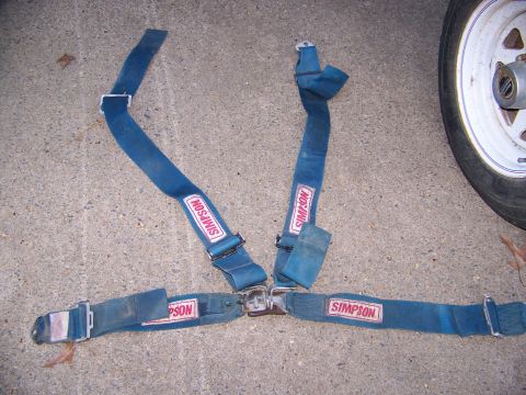 1992 Jeep YJ - A blue Simpson racing harness is laid out on a concrete surface, with a portion of a white wheel and tire visible on the right.