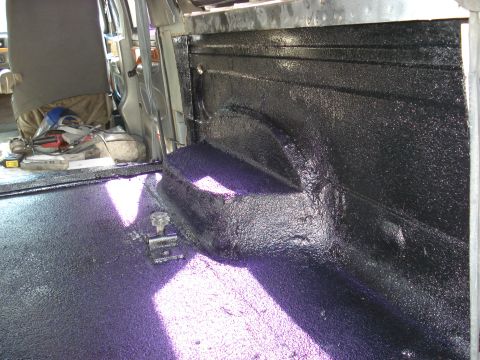 1992 Ford C-350 (Centurion Conversions) - Interior of a vehicle undergoing customization with a black spray-on bed liner applied to the wheel well and side panels.