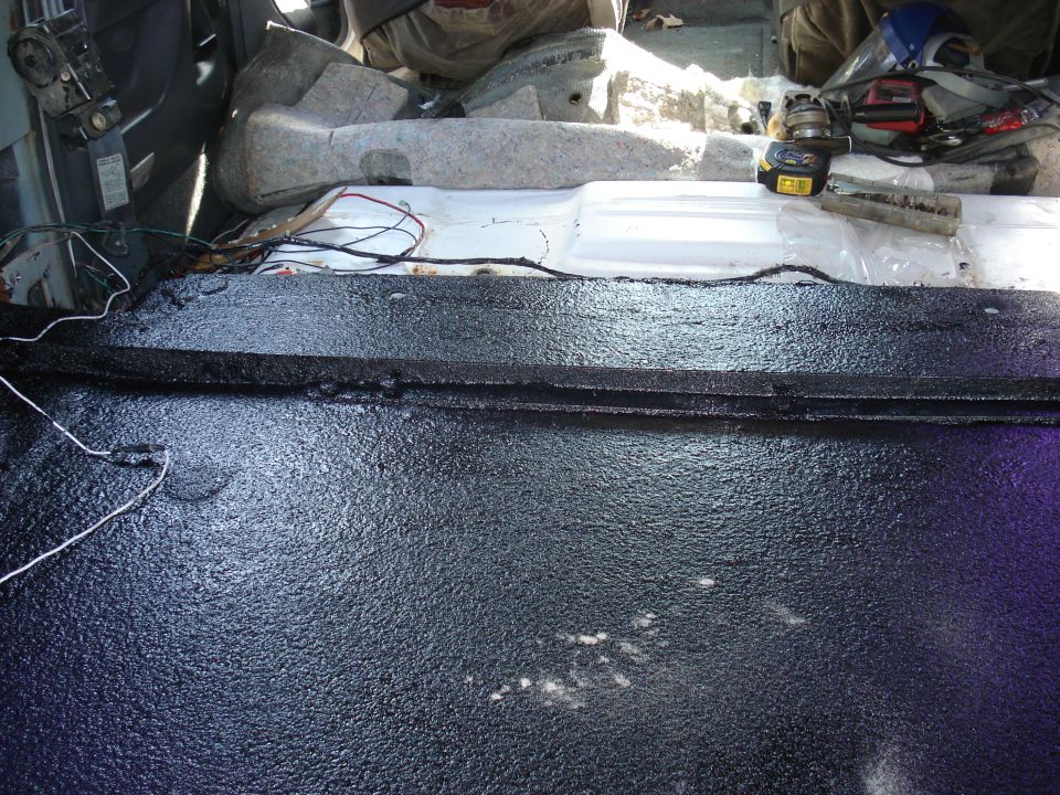 Interior of a vehicle with floor treated with black spray-on bed liner, showing wiring and insulation