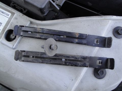 2003 Ford Taurus - Close-up of two headlight mounting brackets, one with a bolt and washer, on a light-colored surface.